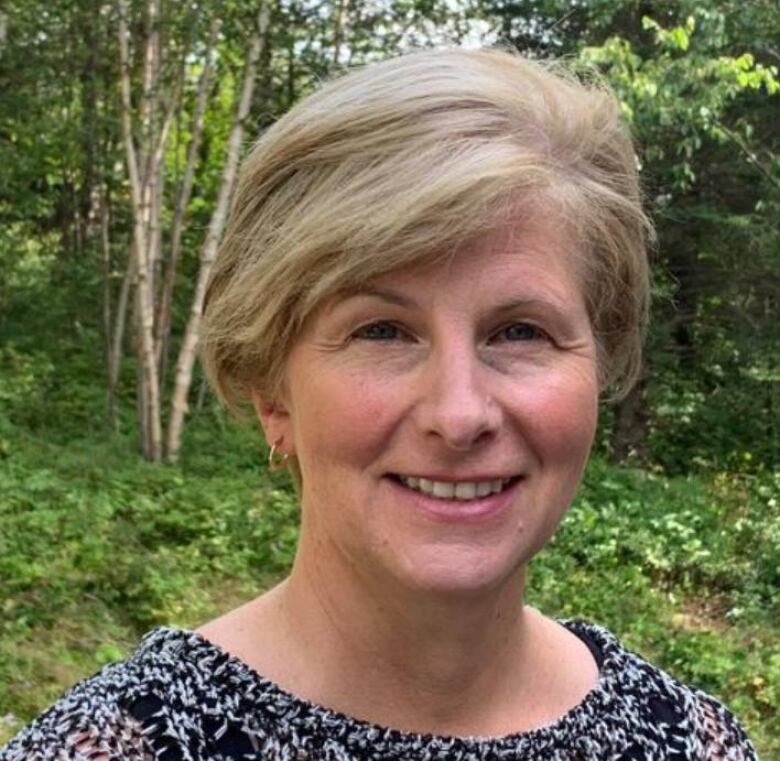 A smiling woman with blonde, chin length hair against a background of birch trees