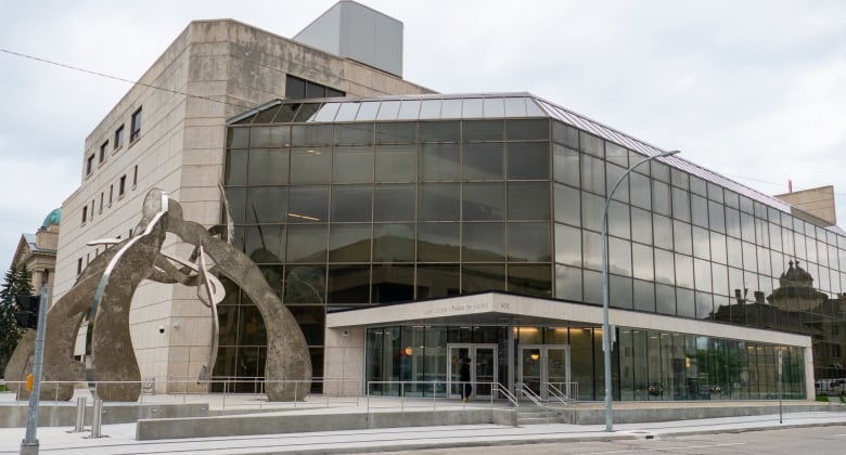 A glass-fronted building features a large piece of public artwork outside the front doors.