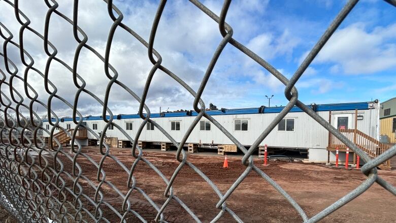 Mobile homes are visible through a gate. THe ground is muddy.