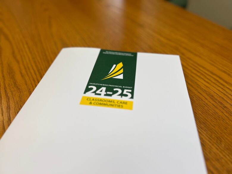 A white hardcover book sits on a wooden table. The booklet has a green and yellow logo and is titled 'Classrooms, Care and Communities.'