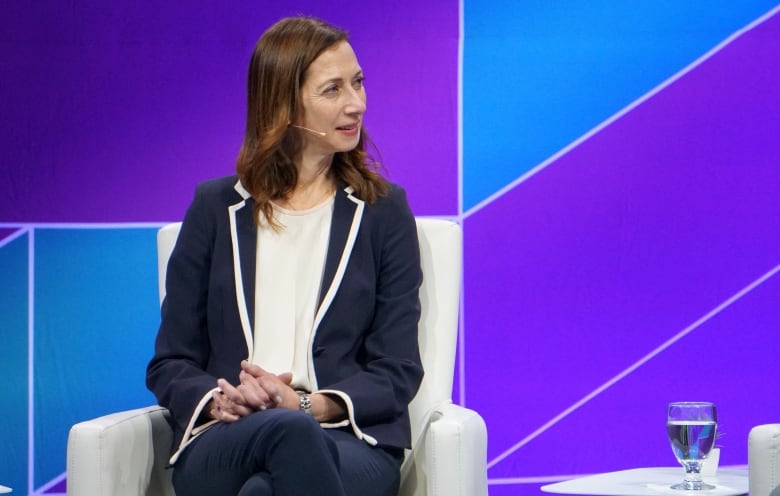 A woman listens while on stage at a conference as part of a panel discussion.