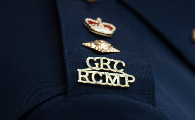 Closeup of a GRC RCMP gold lettering logo and a pin on a navy blue shirt.