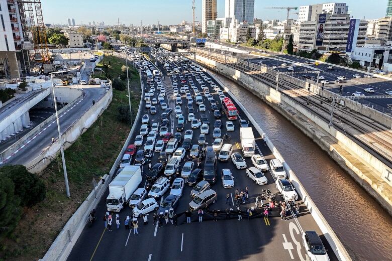 An aerial view of a bridge shows dozens of vehicles behind a line of people holding signs over their head.