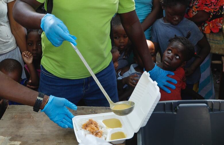 A server ladles soup into a container as children line up to receive food at a shelter for families displaced by gang violence, in Port-au-Prince, Haiti, on March 14.