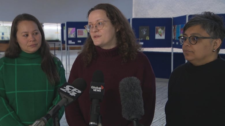 Three women speak in front of microphones.