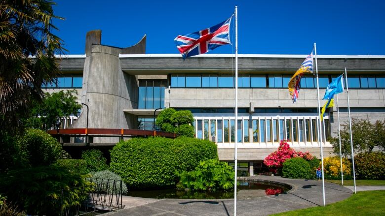 A grey building with rectangular windows and flagpoles out front on a sunny day.