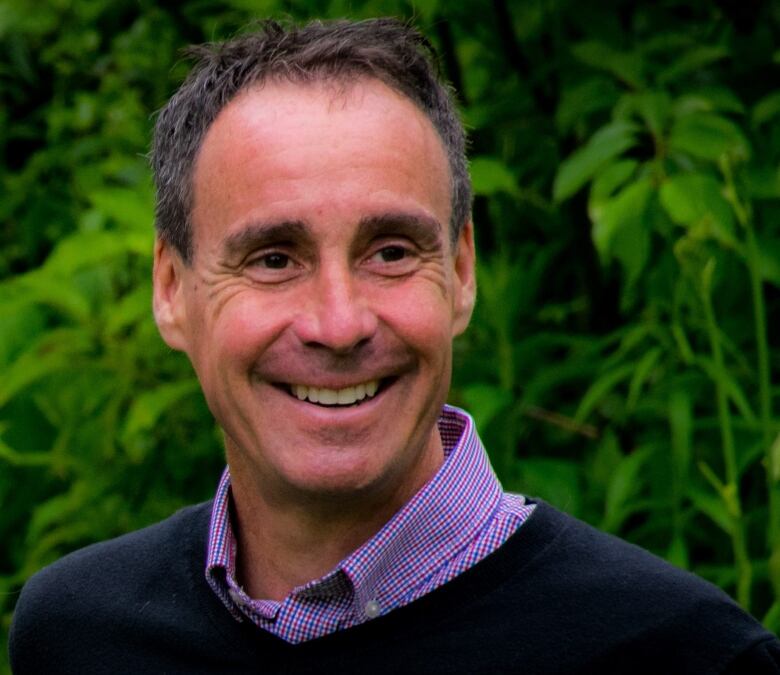 A photo of a smiling man in front of a leafy background