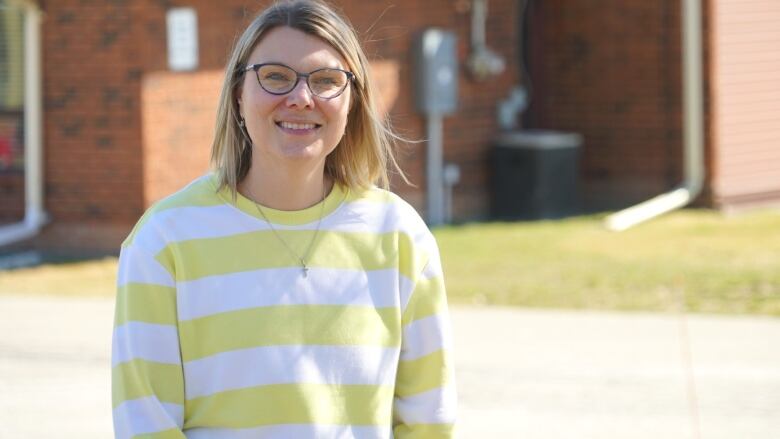 A woman wearing a yellow striped sweatshirt standing outside on a sunny day.