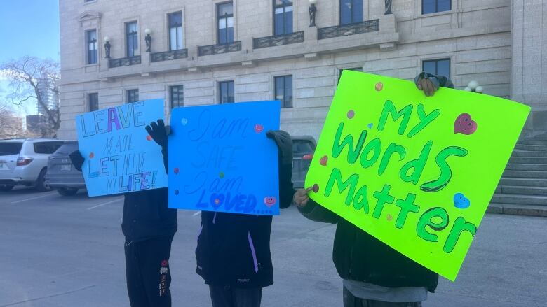 Three children holding a sign over their face. One sign says 