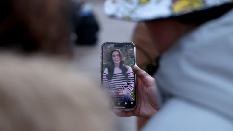 People lean in to watch a video on a phone featuring a woman speaking.