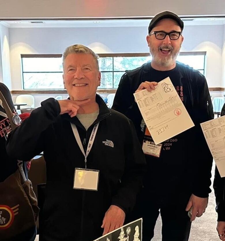 Two men pose for a photo. The man on the right is holding a signed sheet of paper.