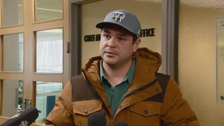 A man in a grey baseball cap speaks to reporters.