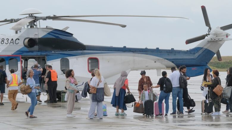 People with luggage stand outside a helicopter at an airport.