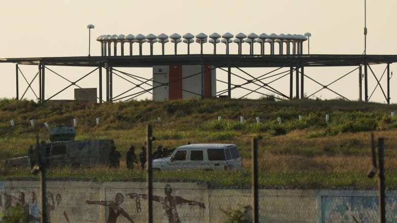 Soldiers, along with military vehicles, stand near a runway at an airport.