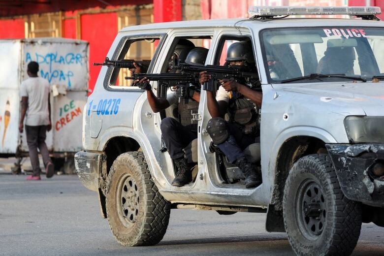 Police officers point their guns as they sit in a a vehicle.