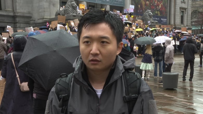 An East Asian man speaks in the background of a large protest.