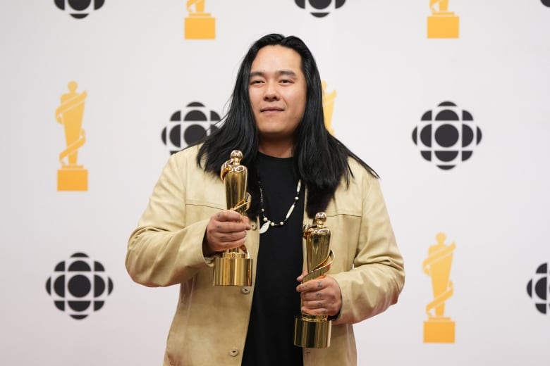 A man holds two golden Juno awards.