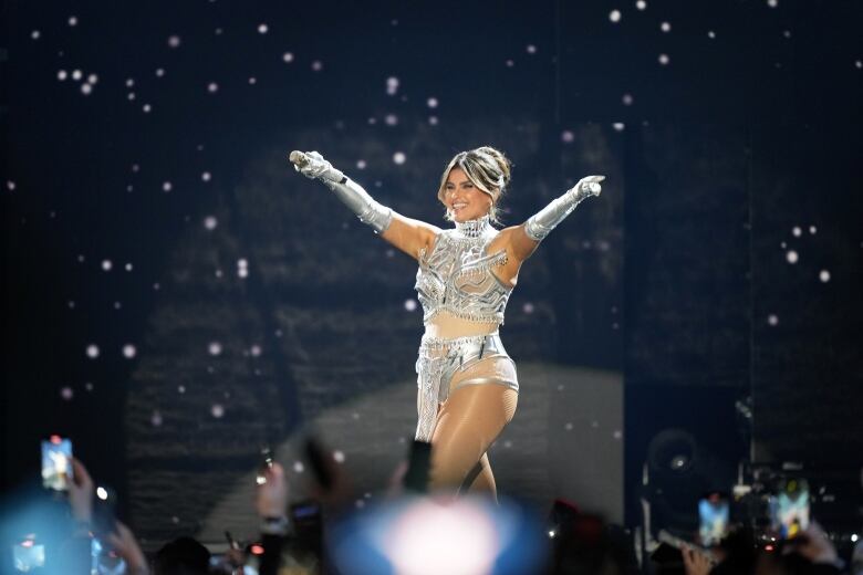 A woman in silver performs on a stage.