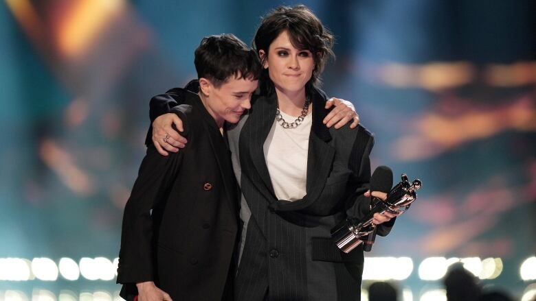 A man leans on the shoulder of a woman holding an award in her hand. 