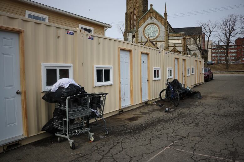 A line of multiple modified shipping containers with small windows and shopping carts parked outside 