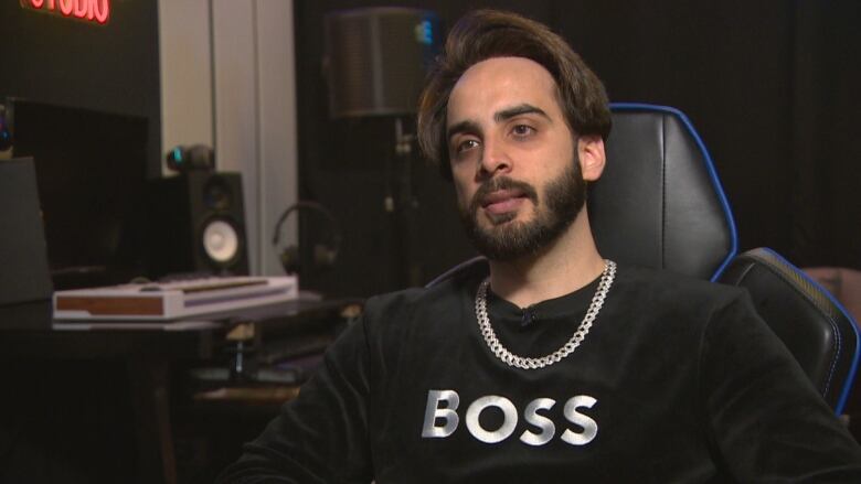 A man sits at a chair in his music studio.