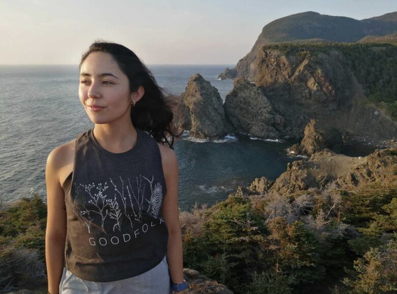 Woman with long black hair, standing with a mountain range in the backdrop