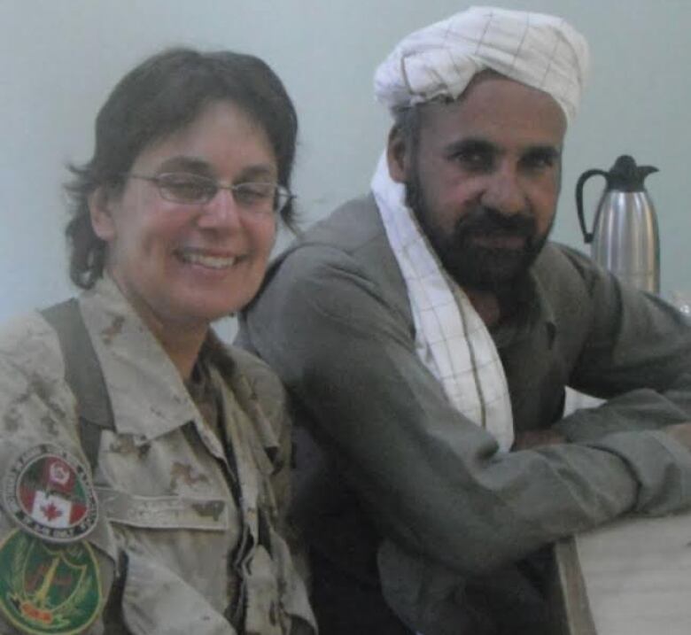 A woman in a Canadian military uniform sits with an Afghan man in his country's traditional clothes.