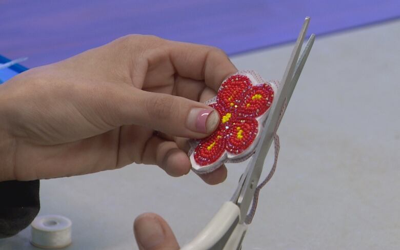 A close up image of hands carefully cutting the leather around the edges of a beaded red and yellow flower. 