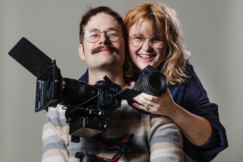 Josh Murphy and Caroline Rex. Josh is holding a video camera and Caroline is holding a camera. 