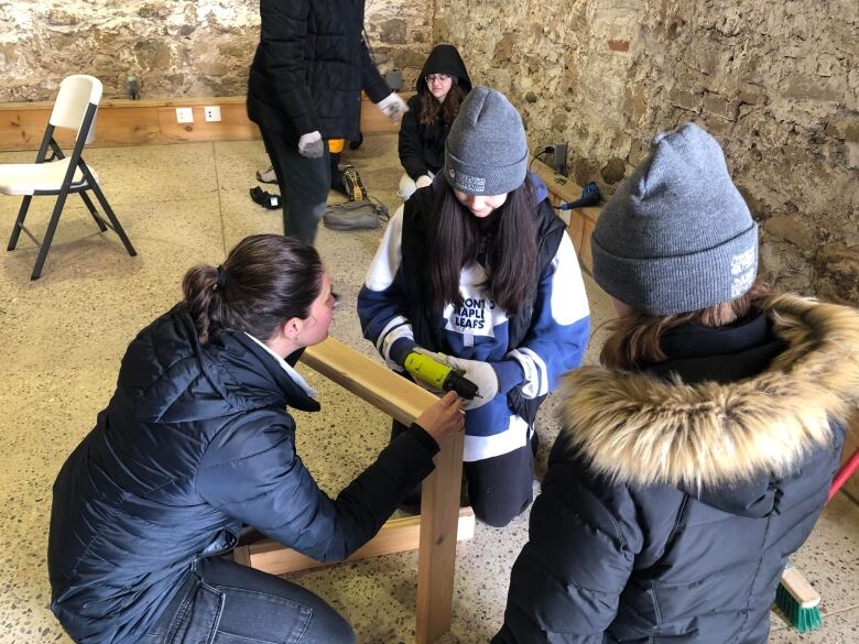 A women helping youth drill screws into wood. 