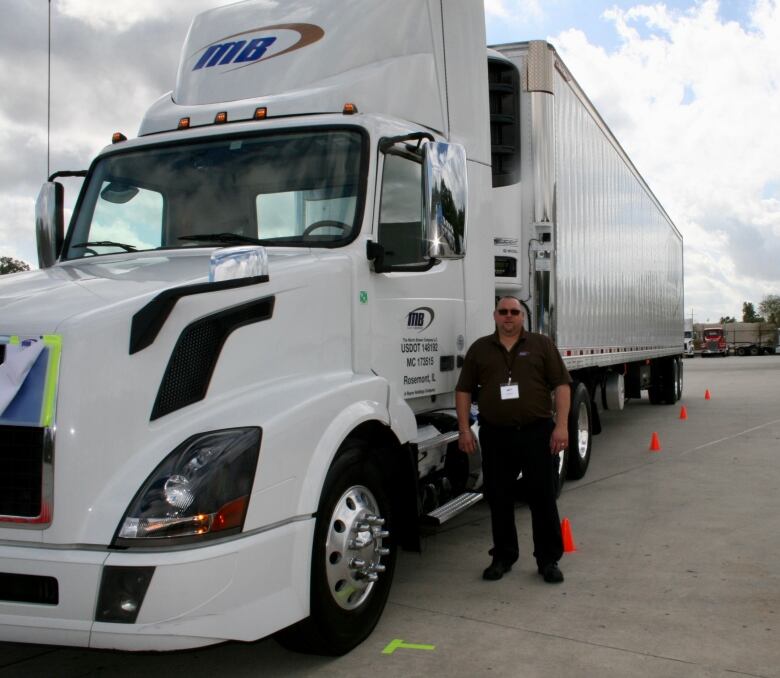 A man dressed in black stands next to a white transport truck.