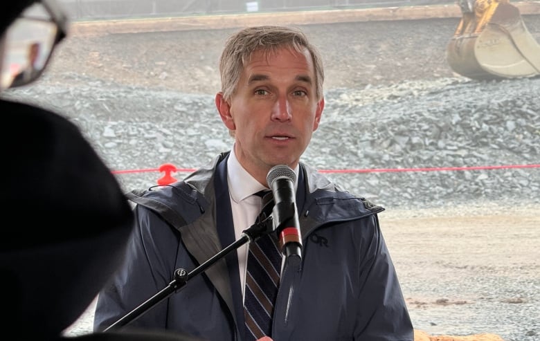 A man wears a blue rain jacket near a construction site.