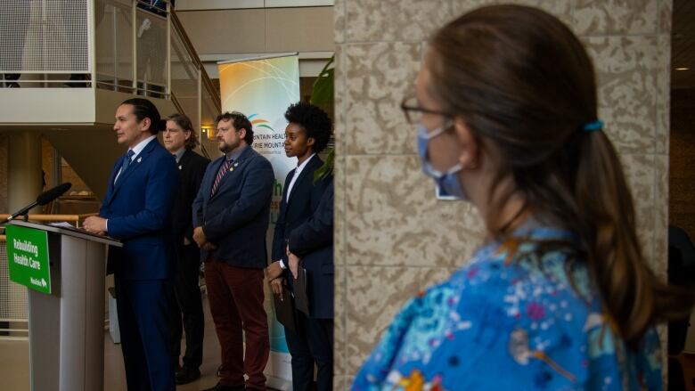 A man stands at a podium as a health care workers watches.