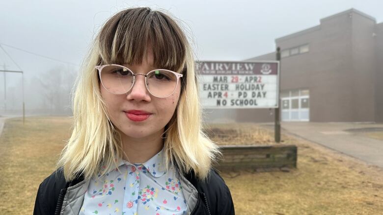 A Halifax Grade 9 student stands in front of the main entrance of her school by a sign that says Fairview Junior High School.