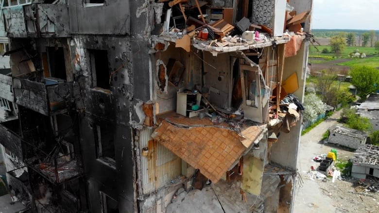 A drone image of a destroyed apartment building, with rooms of an apartment exposed and crumbling. 