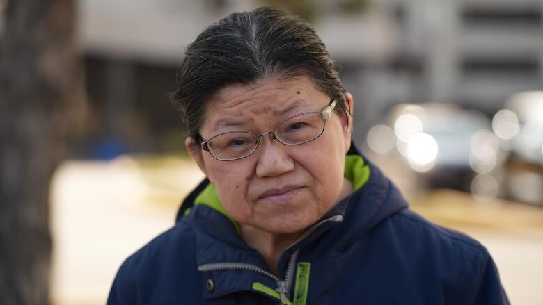 Woman with glasses and a blue coat looks into the camera. 