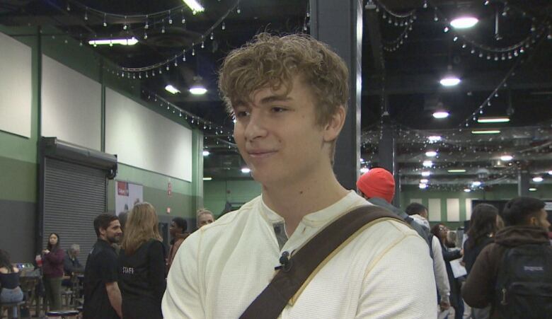 a young man in a white shirt stands in a busy convention centre.