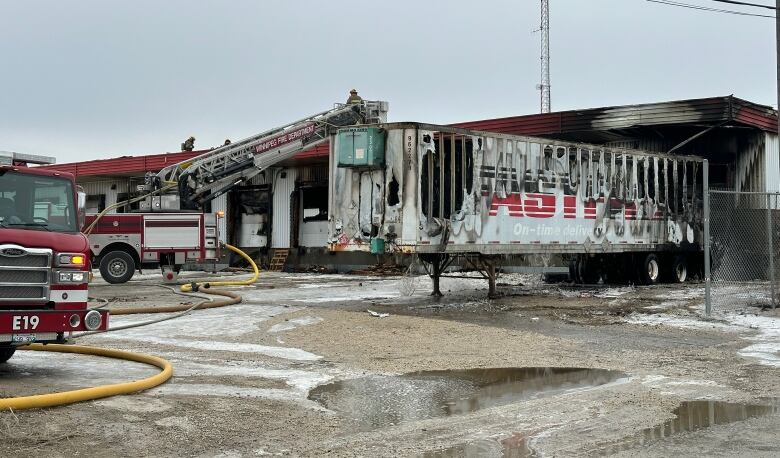 A burnt trailer stands next to a scorched building.