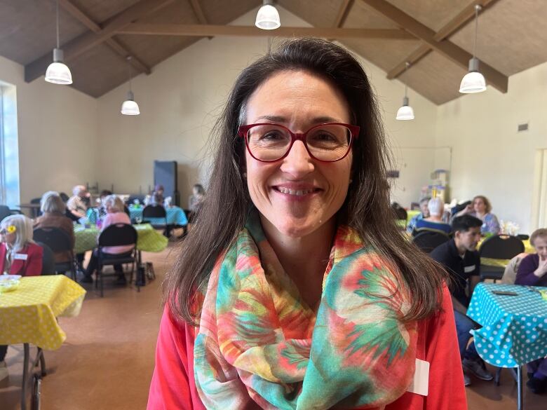 A woman wearing a colourful scarf in a large room filled with seniors. 