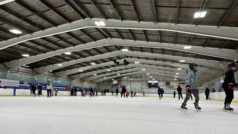 A group of people of all ages skating around an indoor ice rink