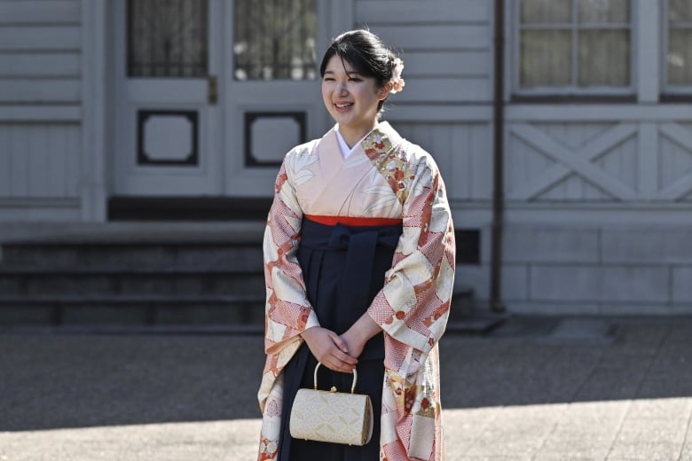 A woman in traditional Japanese clothing smiles in front of a building