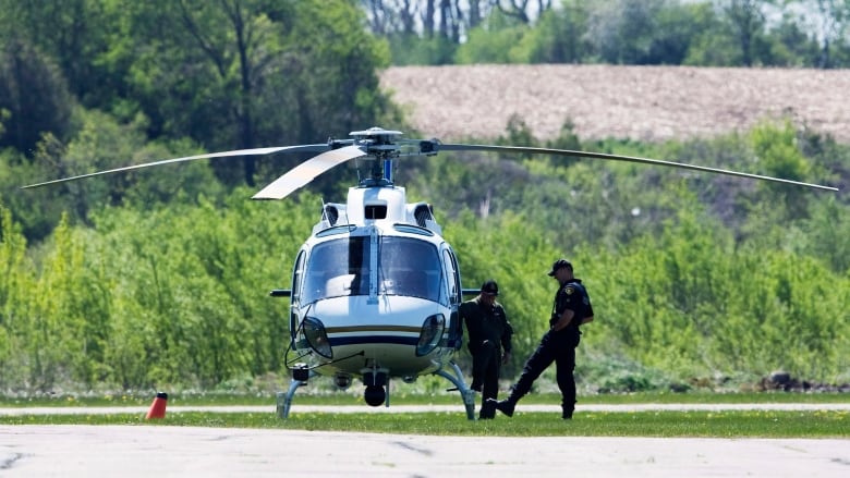 Two police officers stand next to a helicopter on the ground.