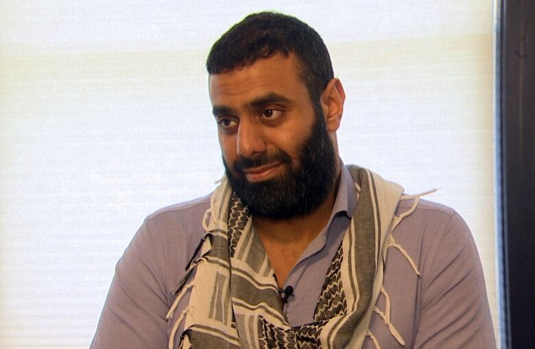 A man with a beard sitting front of an office window. 