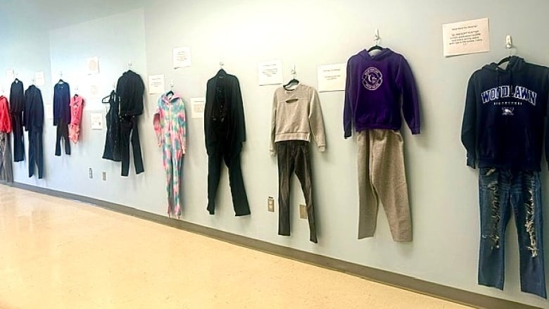 several outfits are seen hung along a wall. beside each outfit is a piece of paper scribing the clothing