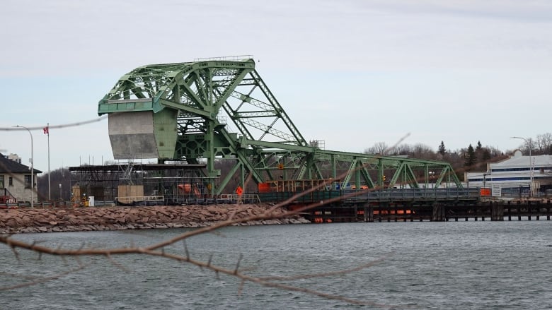 A green, metal bridge, with a large counterweight at one end above choppy water. It's a grey, cloudy day.