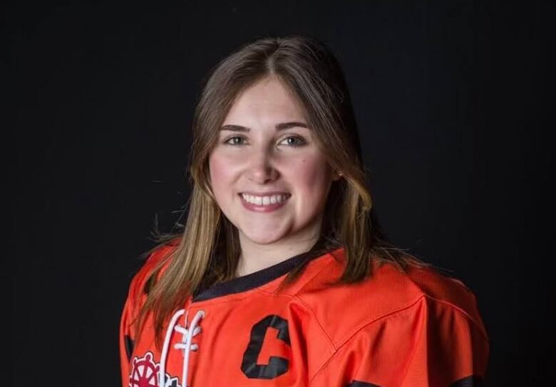 woman with light brown hair, smiling and wearing hockey gear. 