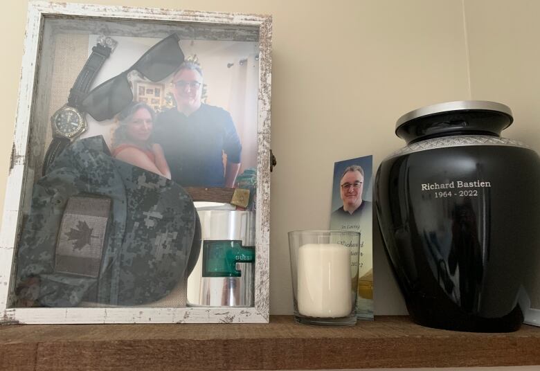 An urn with someone's ashes on a shelf with their picture.