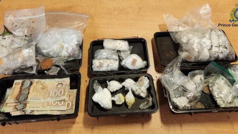 Three black cases with cash and drugs inside. Dirt is on them and the table.