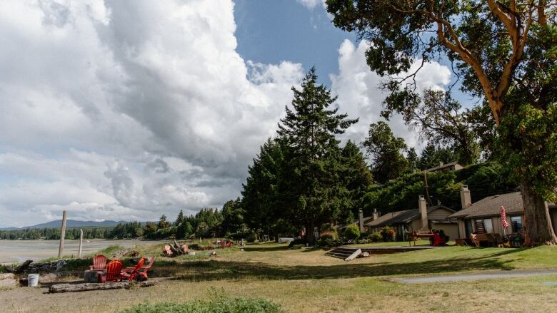 On a hill overlooking a beach, there is a circle of red lawn chairs and a row of small brown houses. 