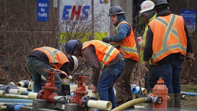 Men in hard hats and reflective vests are show working with yellow pipes.